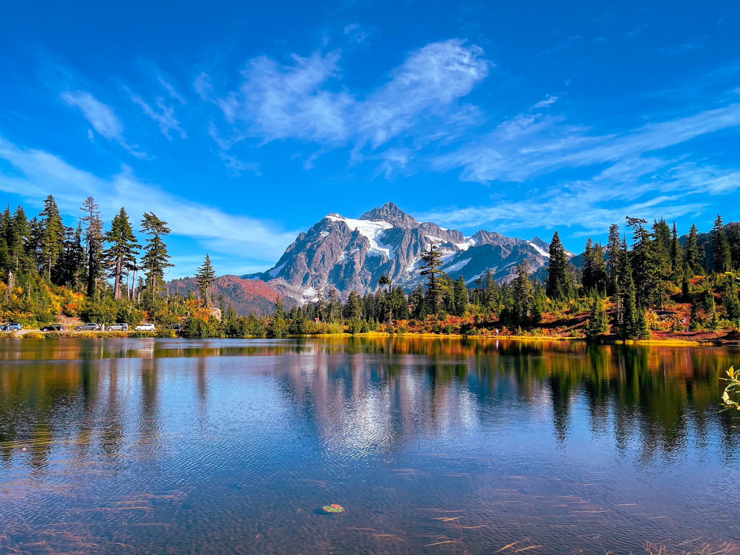 A snow-capped mountain reflected in a still lake surrounded by autumn trees